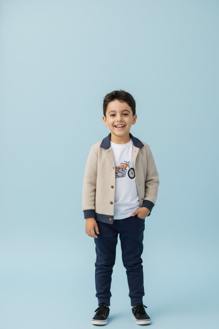 Child wearing a beige jacket, white shirt with graphic design, and dark jeans on a light blue background
